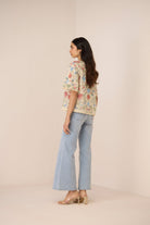 Woman wearing a floral blouse and light blue jeans on a beige background Calling June