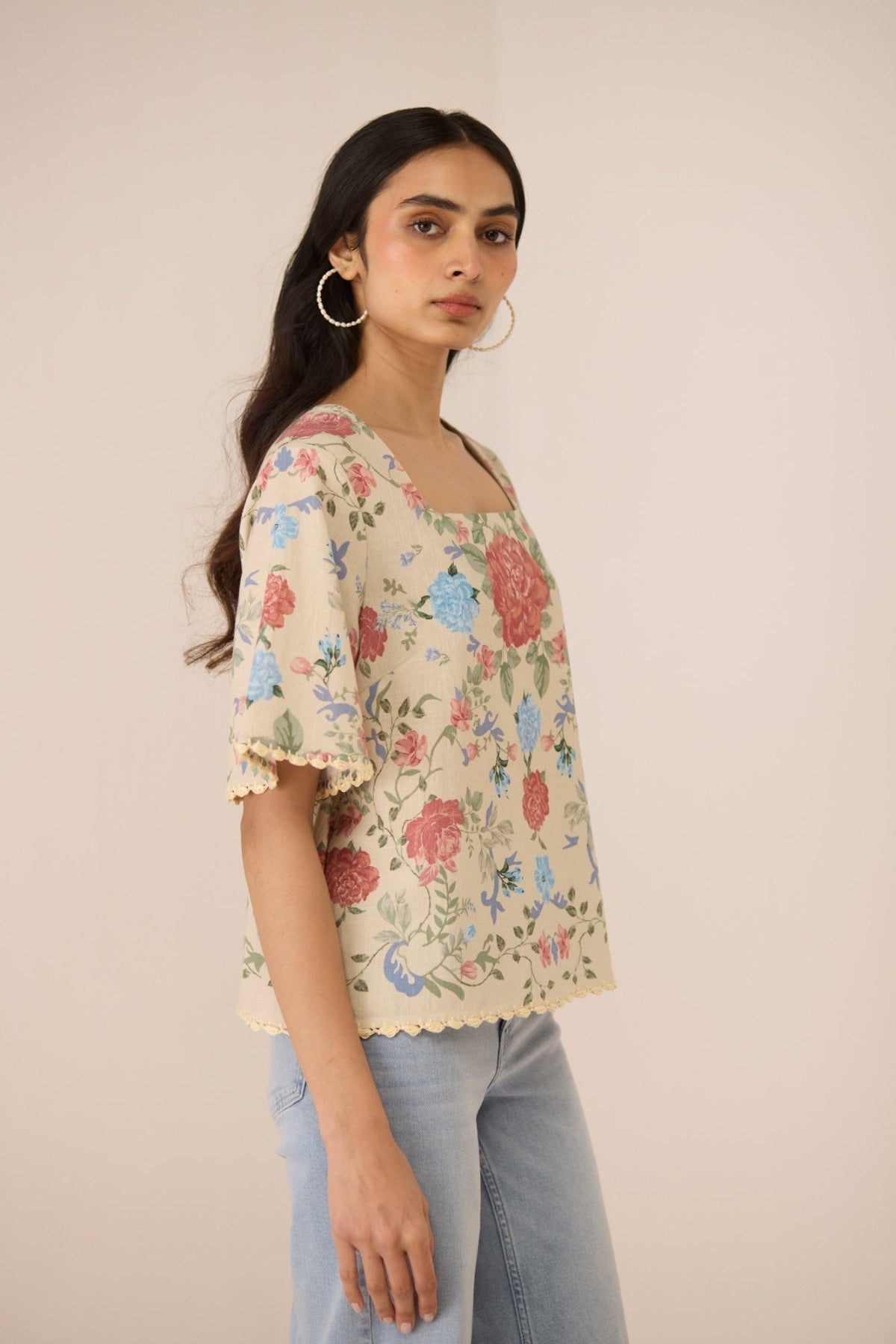 Woman wearing a floral blouse with ruffled sleeves against a beige background Calling June