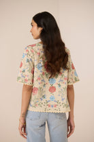 Woman wearing a floral blouse and light blue jeans against a beige background Calling June