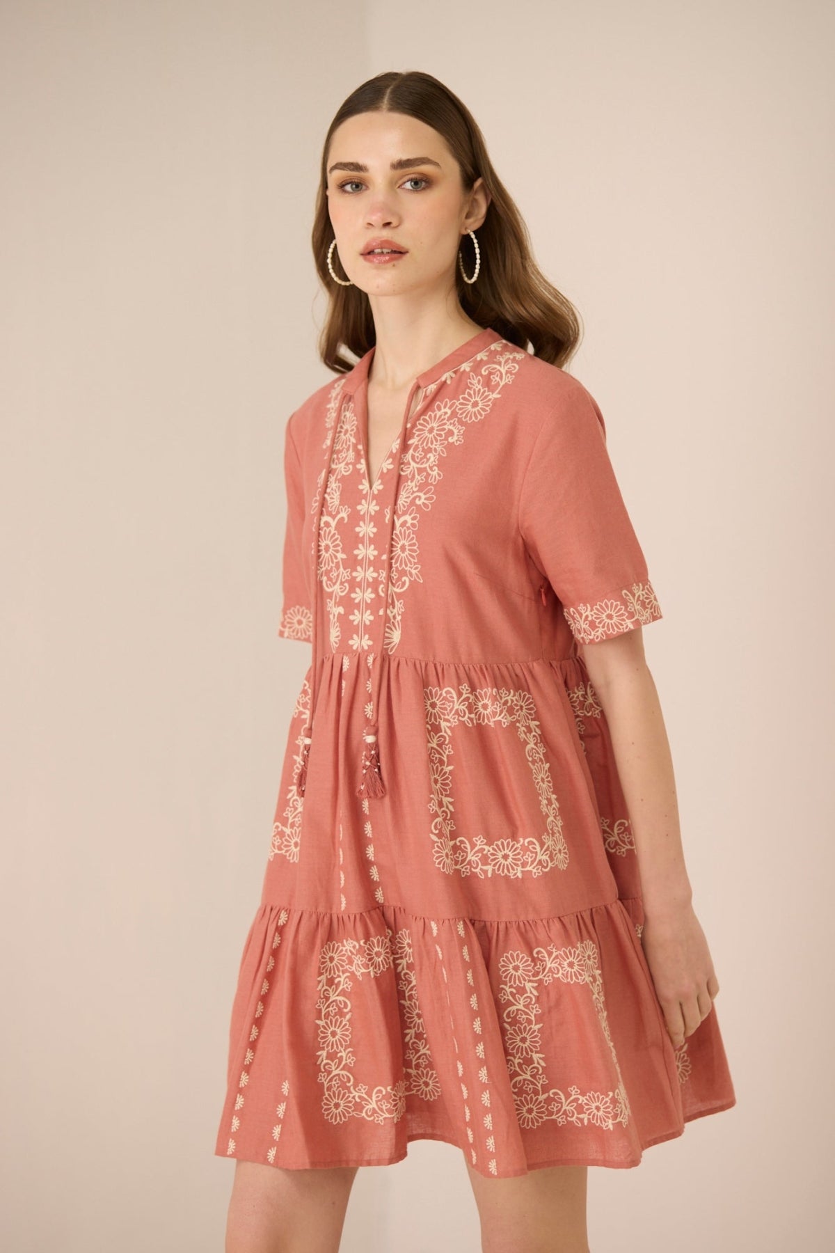 Woman wearing a pink embroidered dress against a beige background Calling June