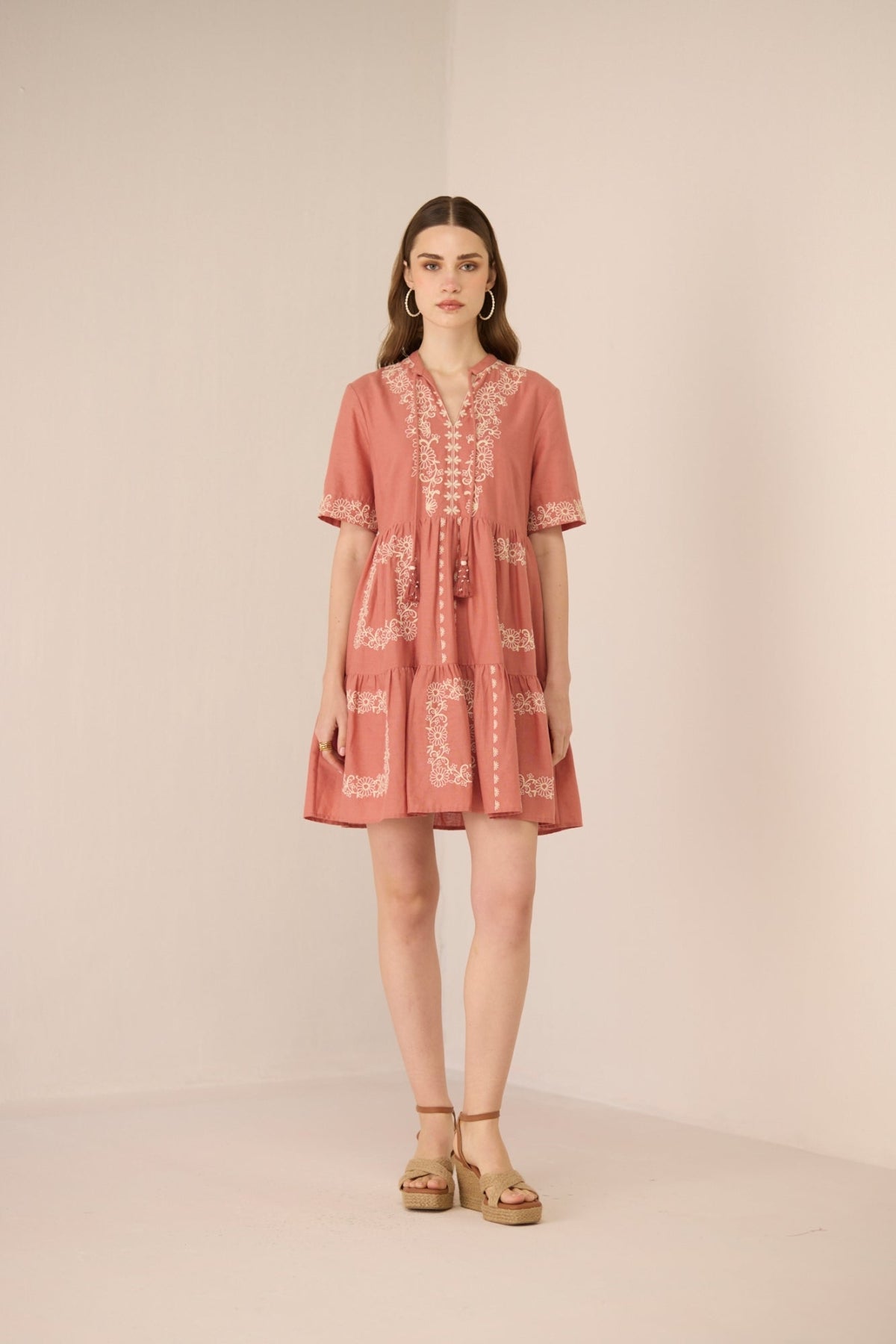 Woman wearing a pink dress with white embroidery on a beige background Calling June