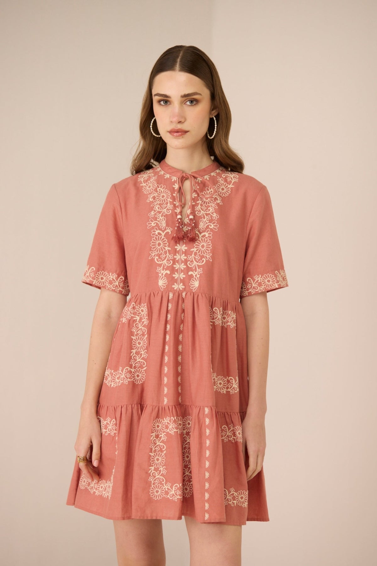 Woman wearing a pink dress with white embroidery on a beige background Calling June