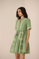 Woman wearing a green dress with floral embroidery against a beige background Calling June