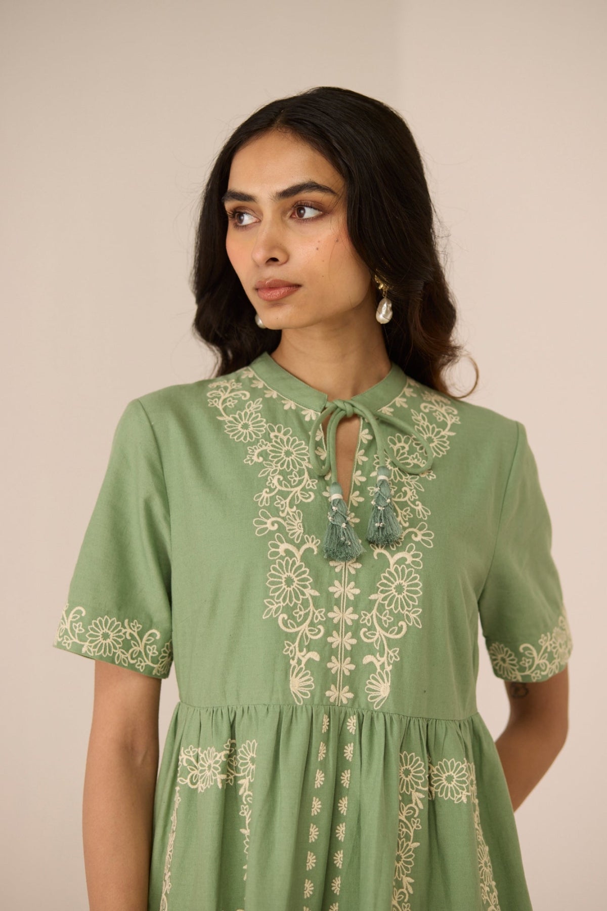 Woman wearing a green dress with floral embroidery against a beige background Calling June