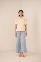 Woman wearing a light yellow blouse with short sleeves and light blue jeans on a beige background Calling June