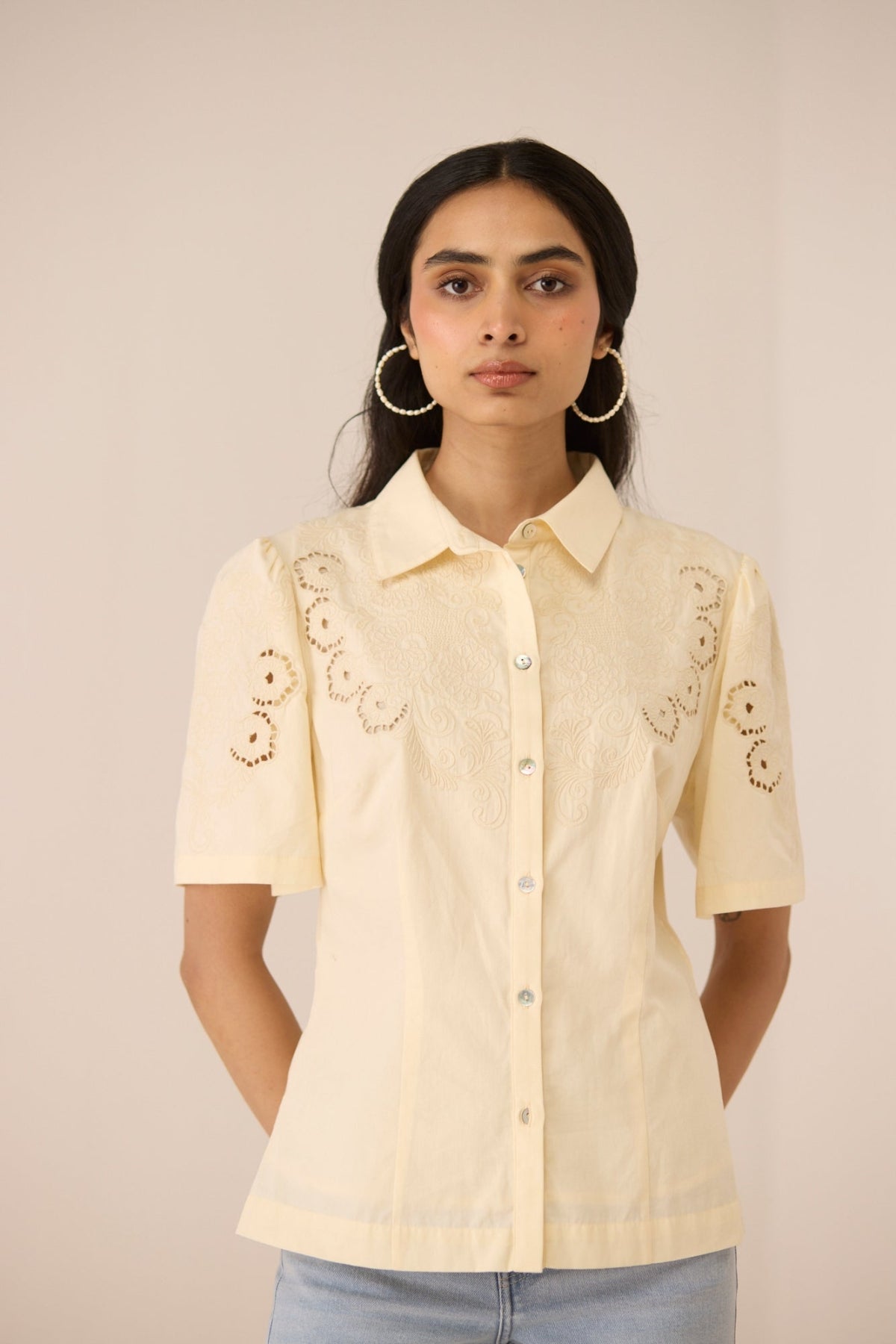 Woman wearing a cream-colored shirt with floral embroidery on a beige background Calling June 