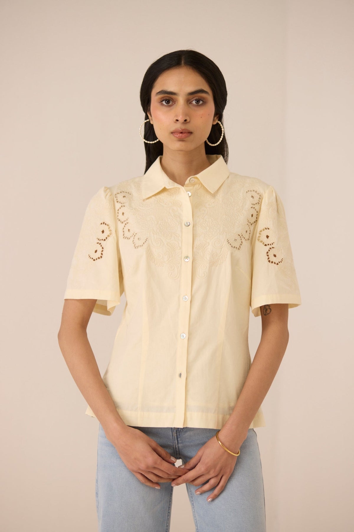 Woman wearing a light yellow embroidered shirt against a beige background Calling June