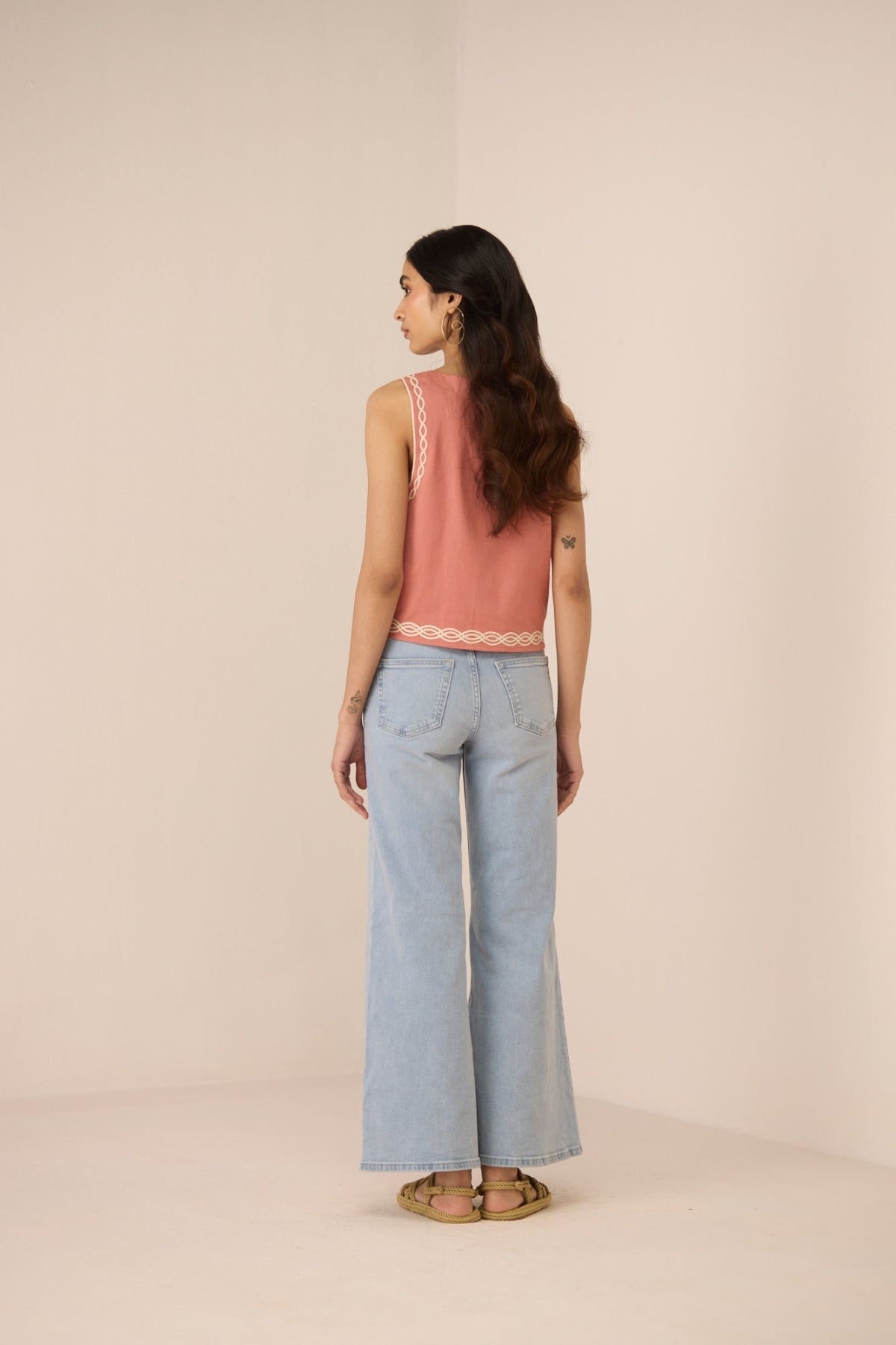 Woman wearing a pink sleeveless top and light blue jeans on a beige background Calling June