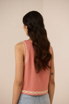 Woman wearing a pink sleeveless top with decorative back straps against a beige background Calling June