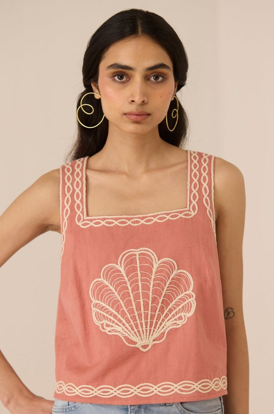 Woman wearing a pink tank top with shell design and lace details on a beige background Calling June