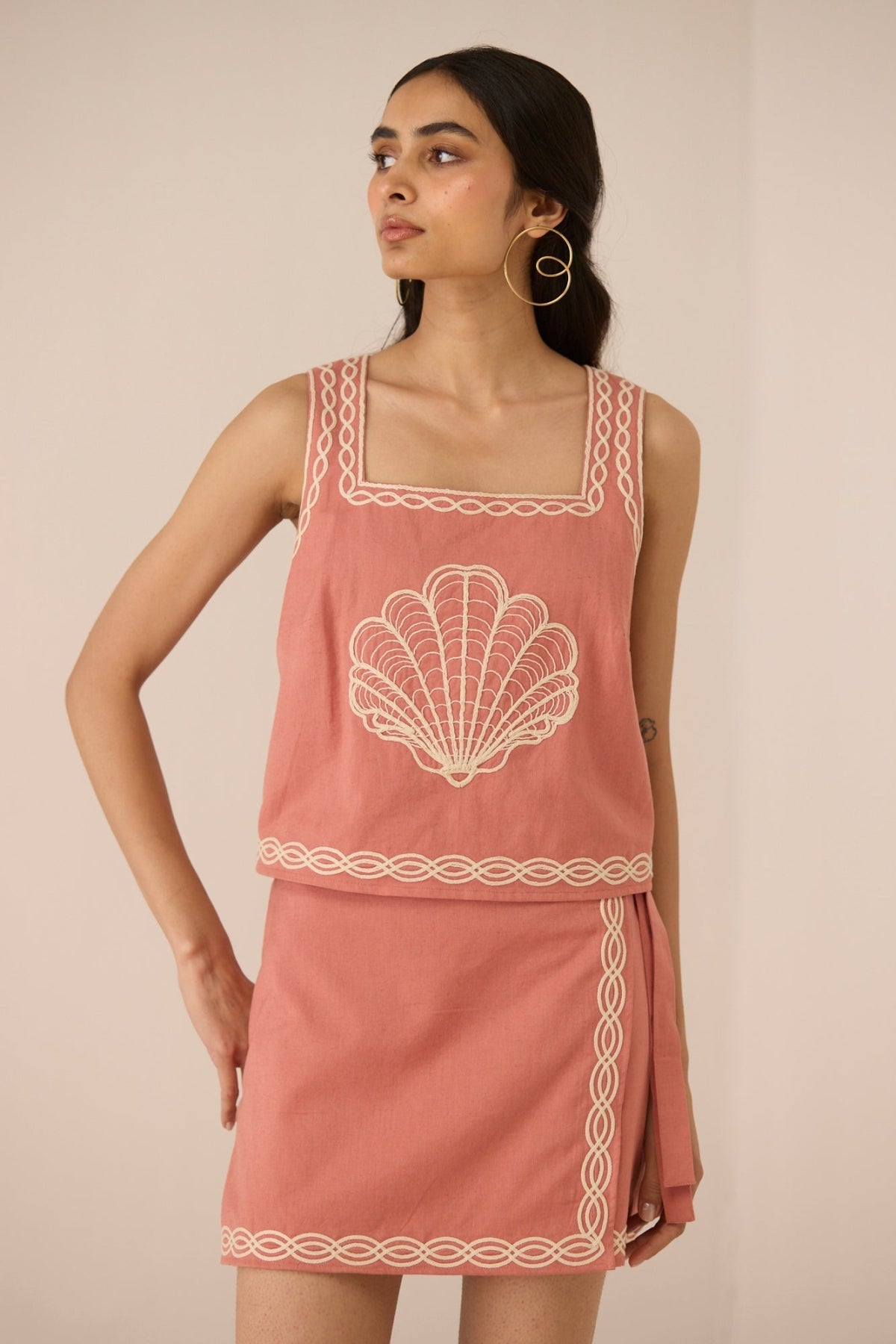 Woman wearing a pink dress with shell design on a beige background Calling June