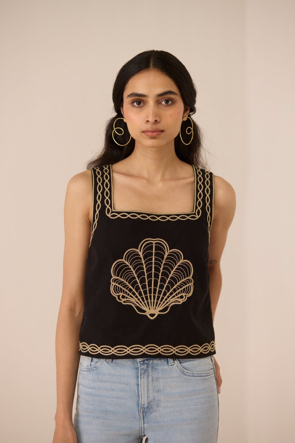 Woman wearing a black sleeveless top with gold embroidery against a beige background Calling June