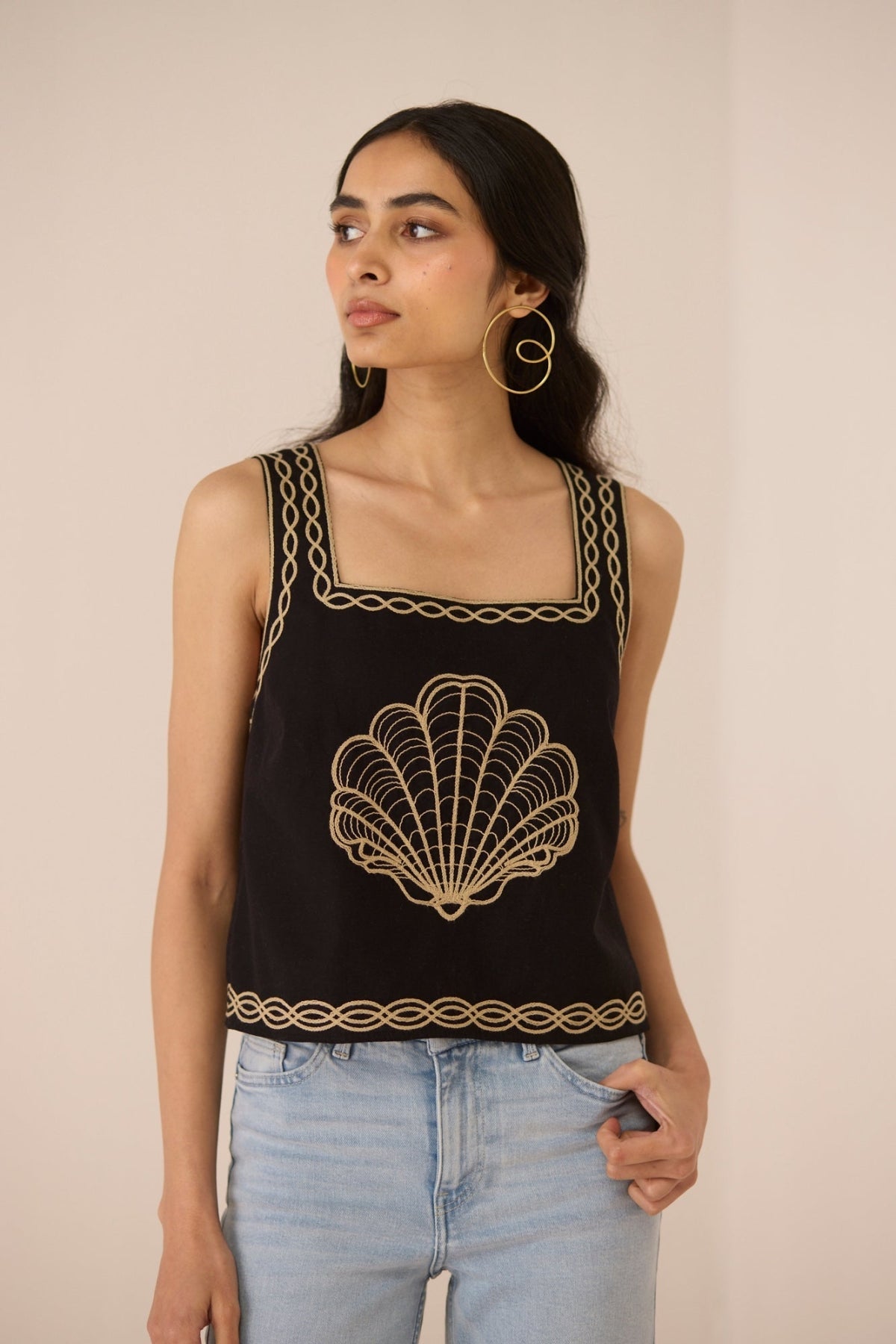 Woman wearing a black tank top with gold embroidery against a beige background Calling June