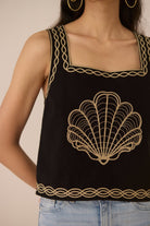 Black top with gold shell design and trim worn by a person Calling June