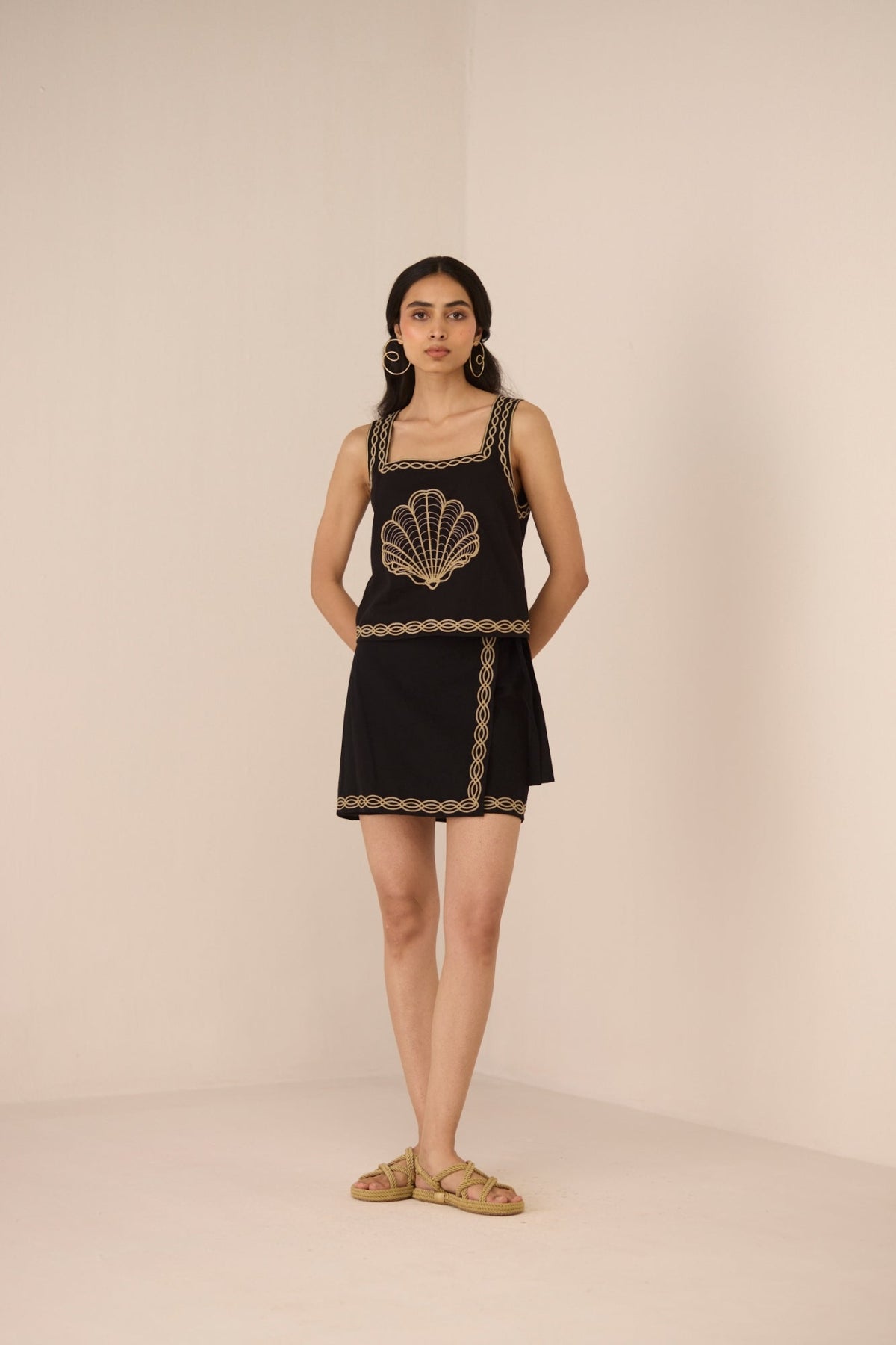 Woman wearing a black dress with gold embroidery against a beige background Calling June