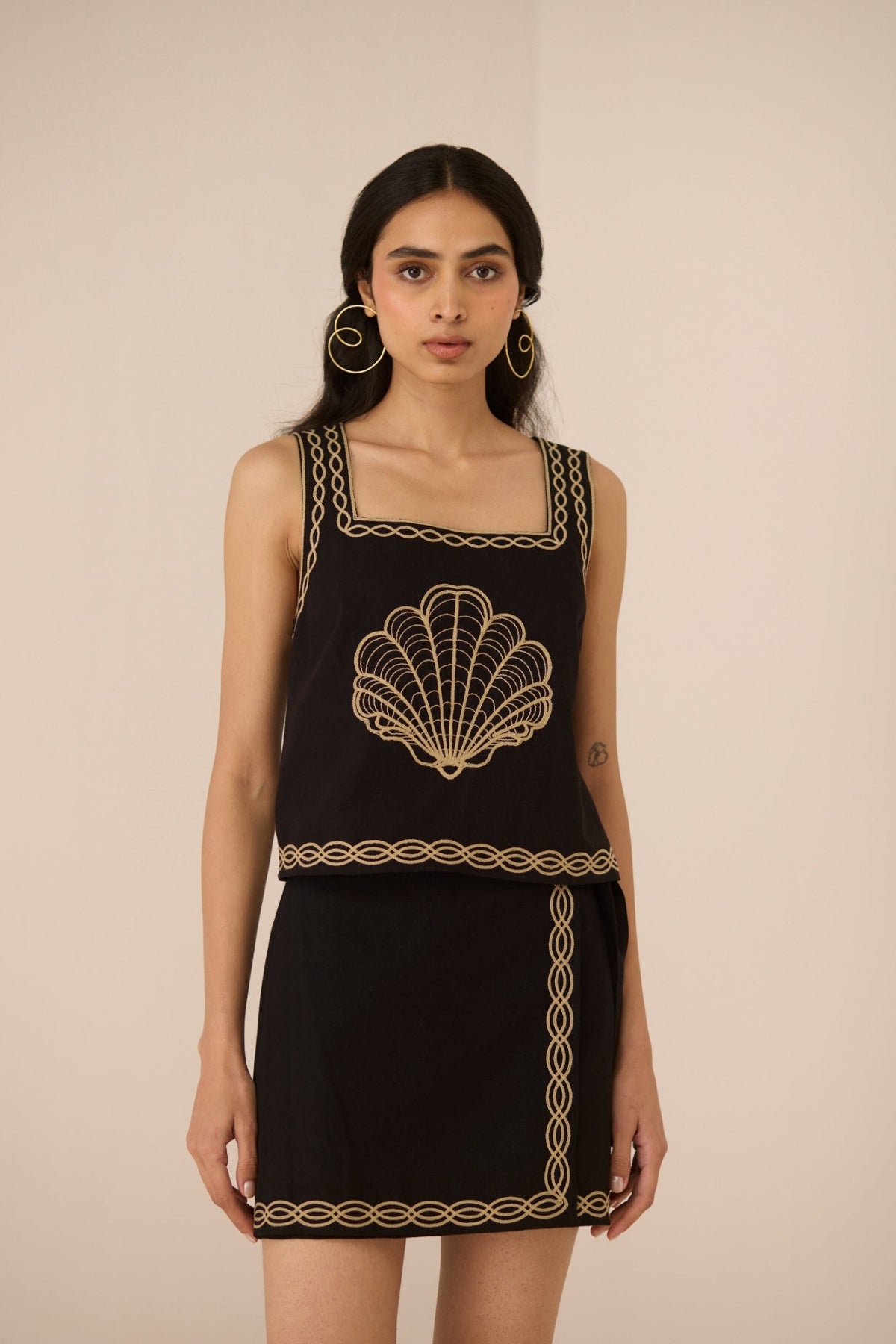 Woman wearing a black dress with gold embroidery on a beige background Calling June