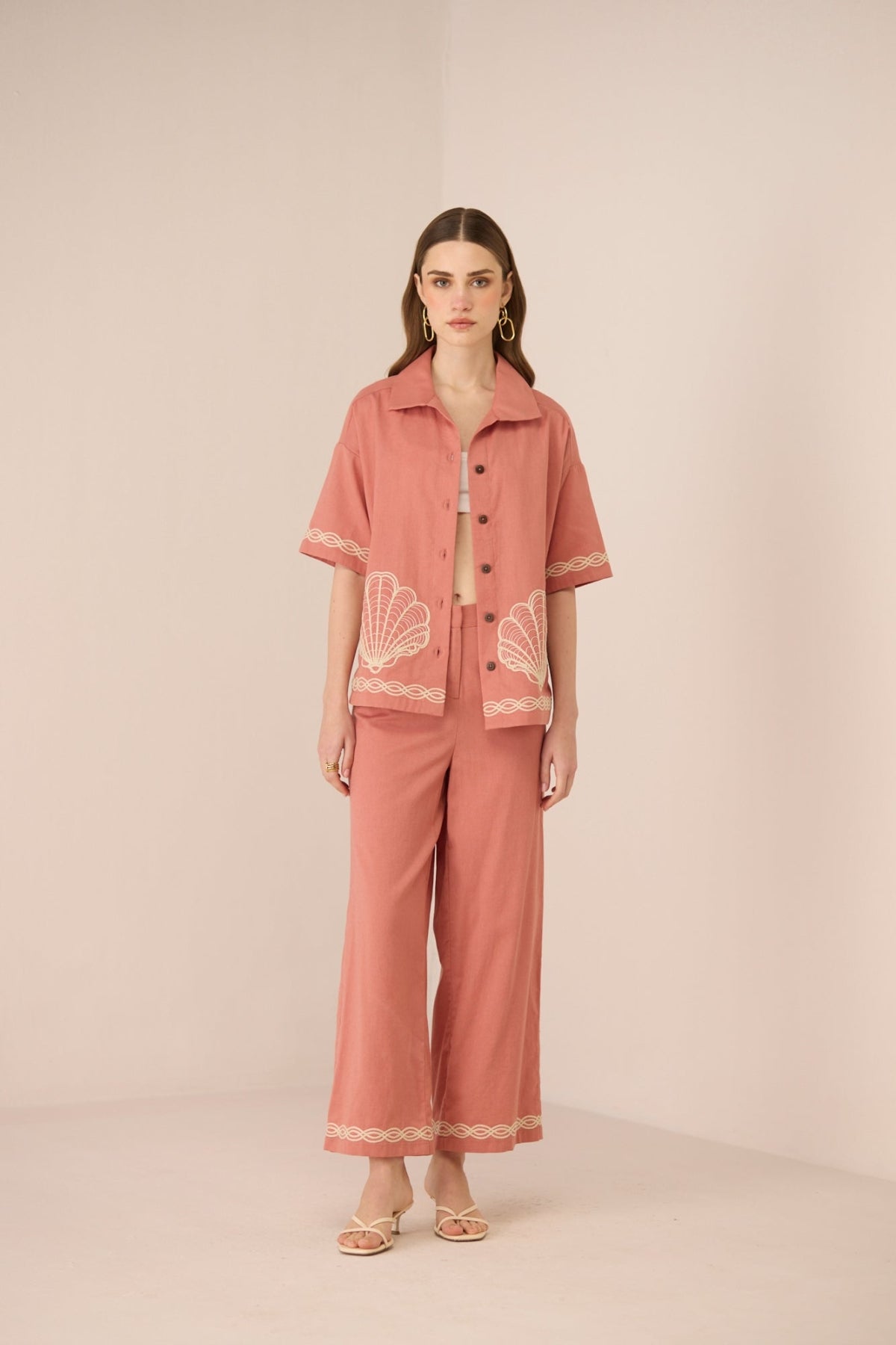 Woman wearing a pink outfit with shell patterns on a beige background Calling June