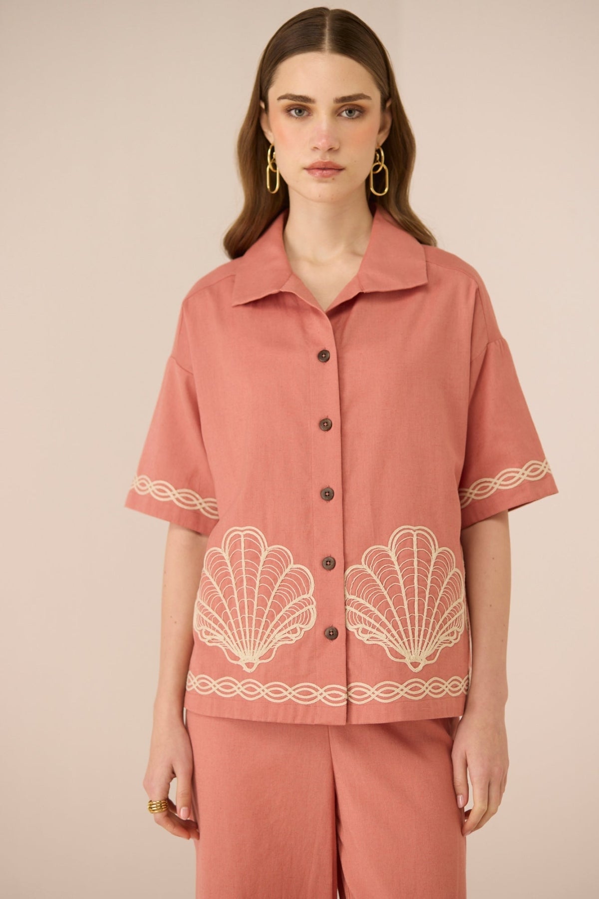 Woman wearing a pink blouse with shell patterns on a beige background Calling June
