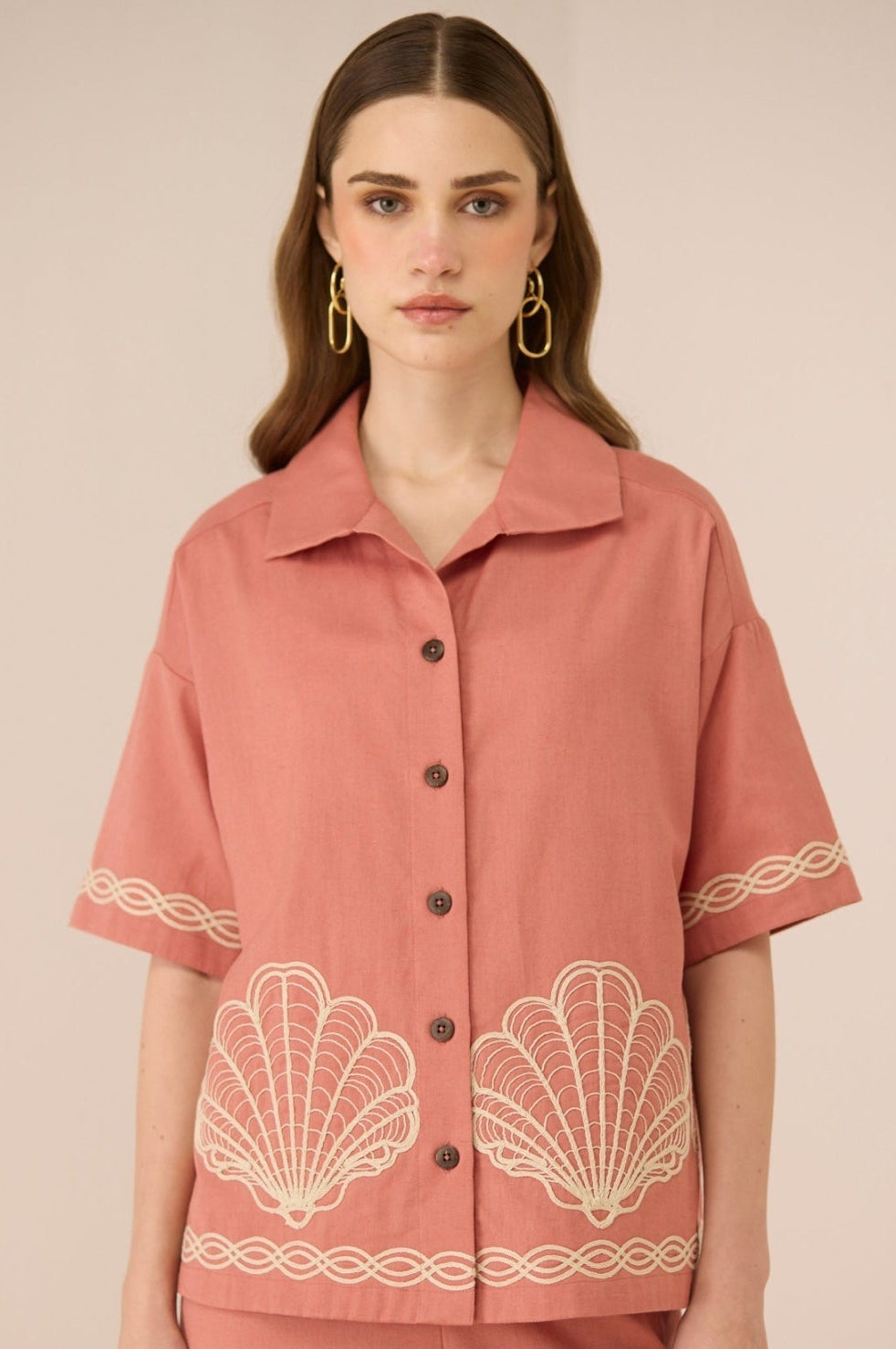 Woman wearing a pink blouse with shell patterns on a beige background Calling June