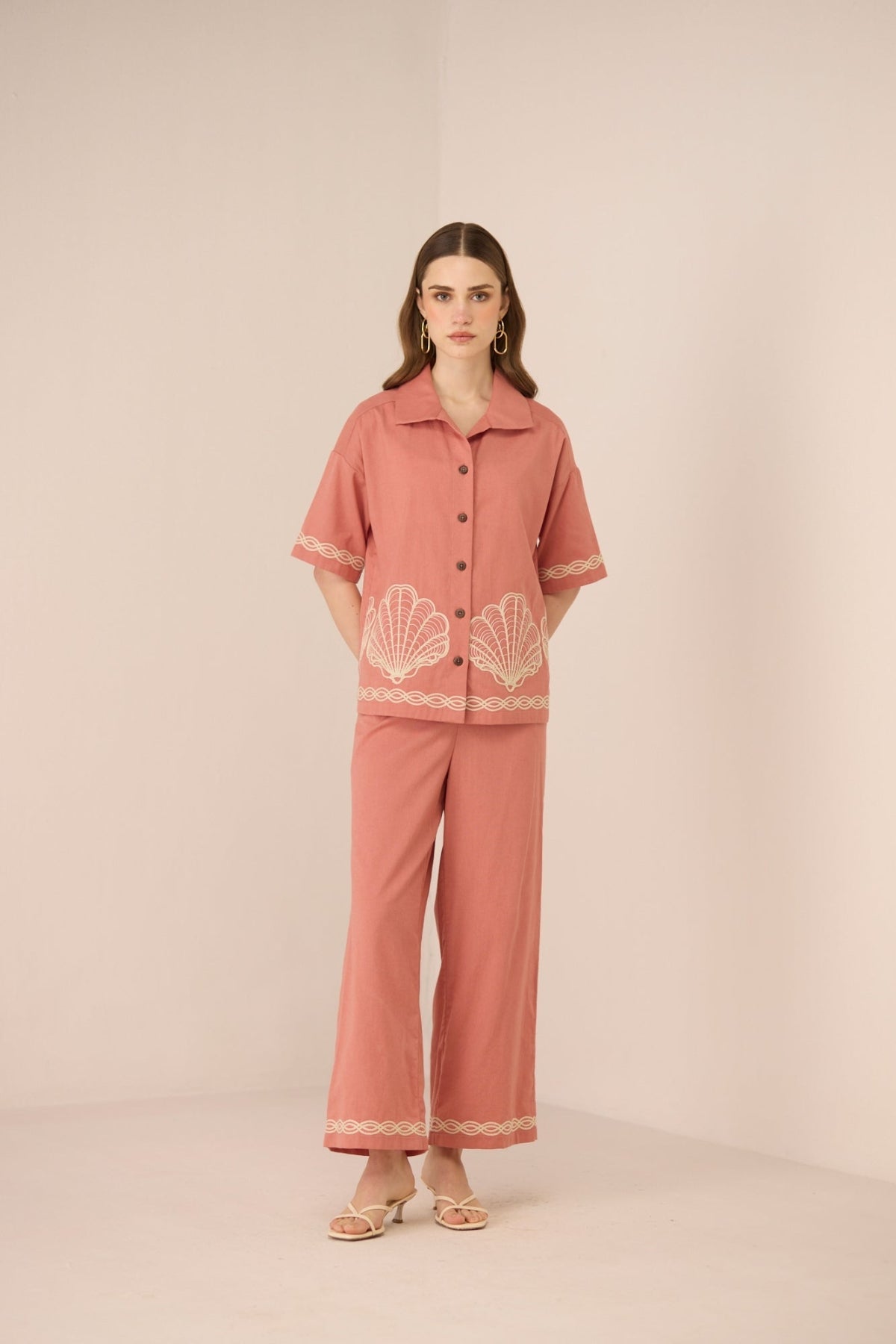 Woman wearing a pink outfit with shell embroidery on a beige background Calling June