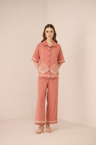 Woman wearing a pink outfit with shell embroidery on a beige background Calling June