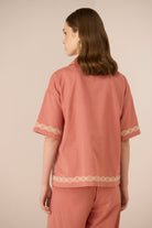 Person wearing a pink outfit with white embroidery on a beige background Calling June