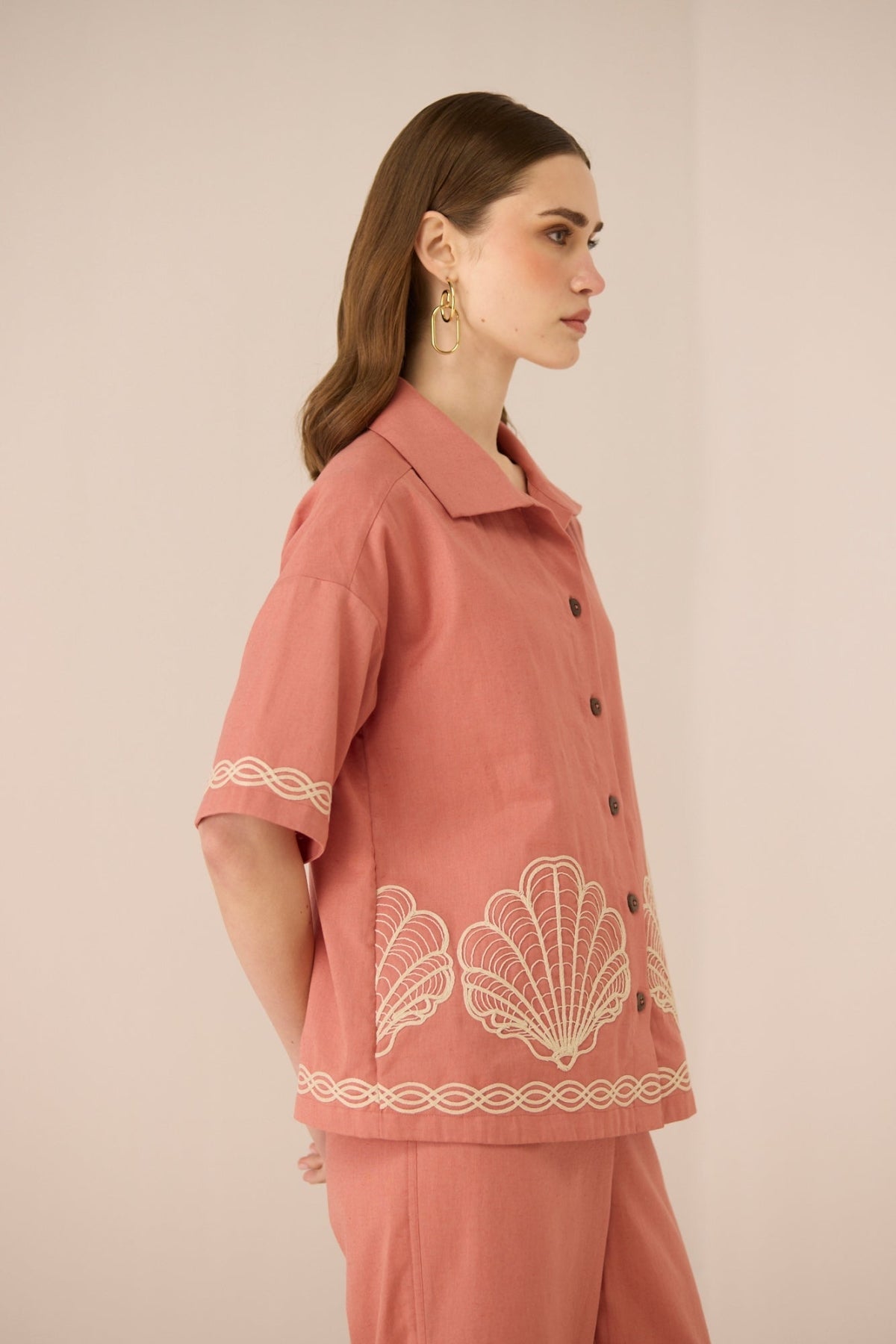 Woman wearing a pink outfit with white embroidery on a beige background Calling June