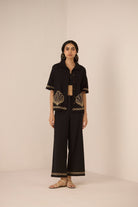 Woman wearing a black outfit with gold embroidery on a beige background Calling June