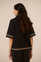 Woman wearing a black blouse with gold embroidery on a beige background Calling June