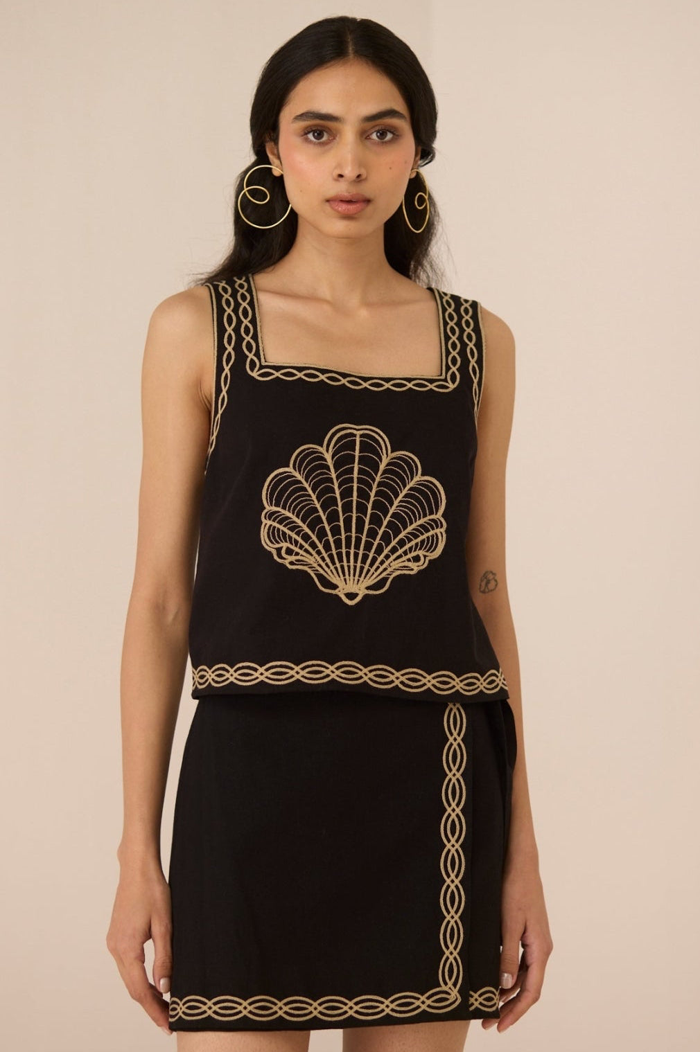 Woman wearing a black dress with gold embroidery on a beige background Calling June