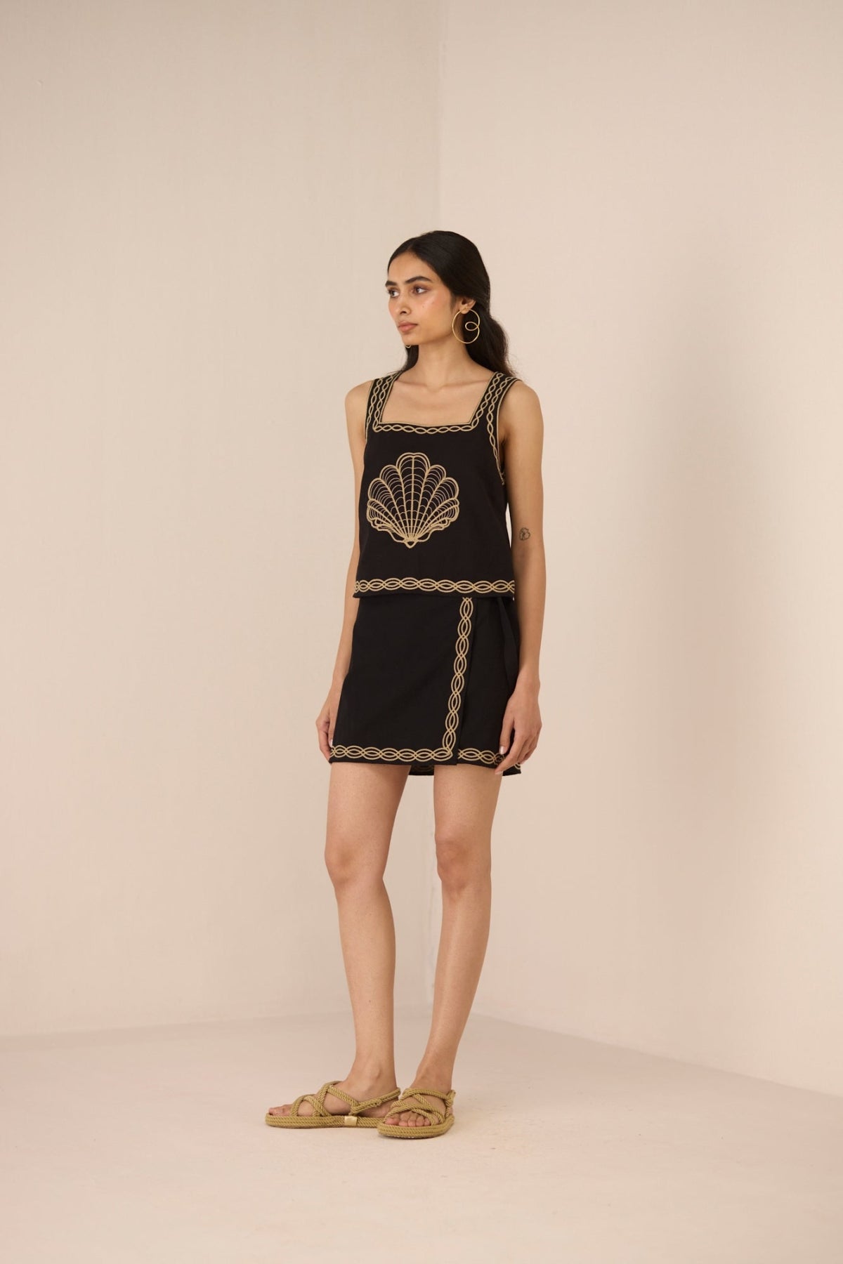 Woman wearing a black dress with gold embroidery on a beige background Calling June