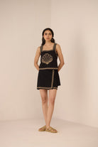 Woman wearing a black dress with gold embroidery against a beige background Calling June