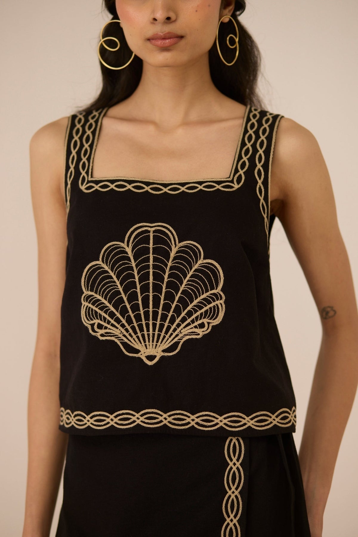 Black sleeveless top with gold embroidery on a plain background Calling June