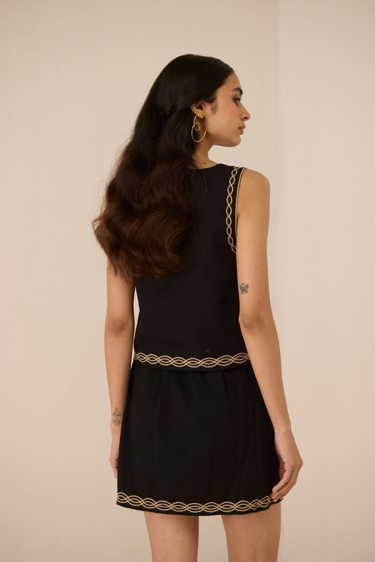 Woman wearing a black dress with gold trim on a beige background Calling June