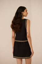 Woman wearing a black dress with gold trim on a beige background Calling June