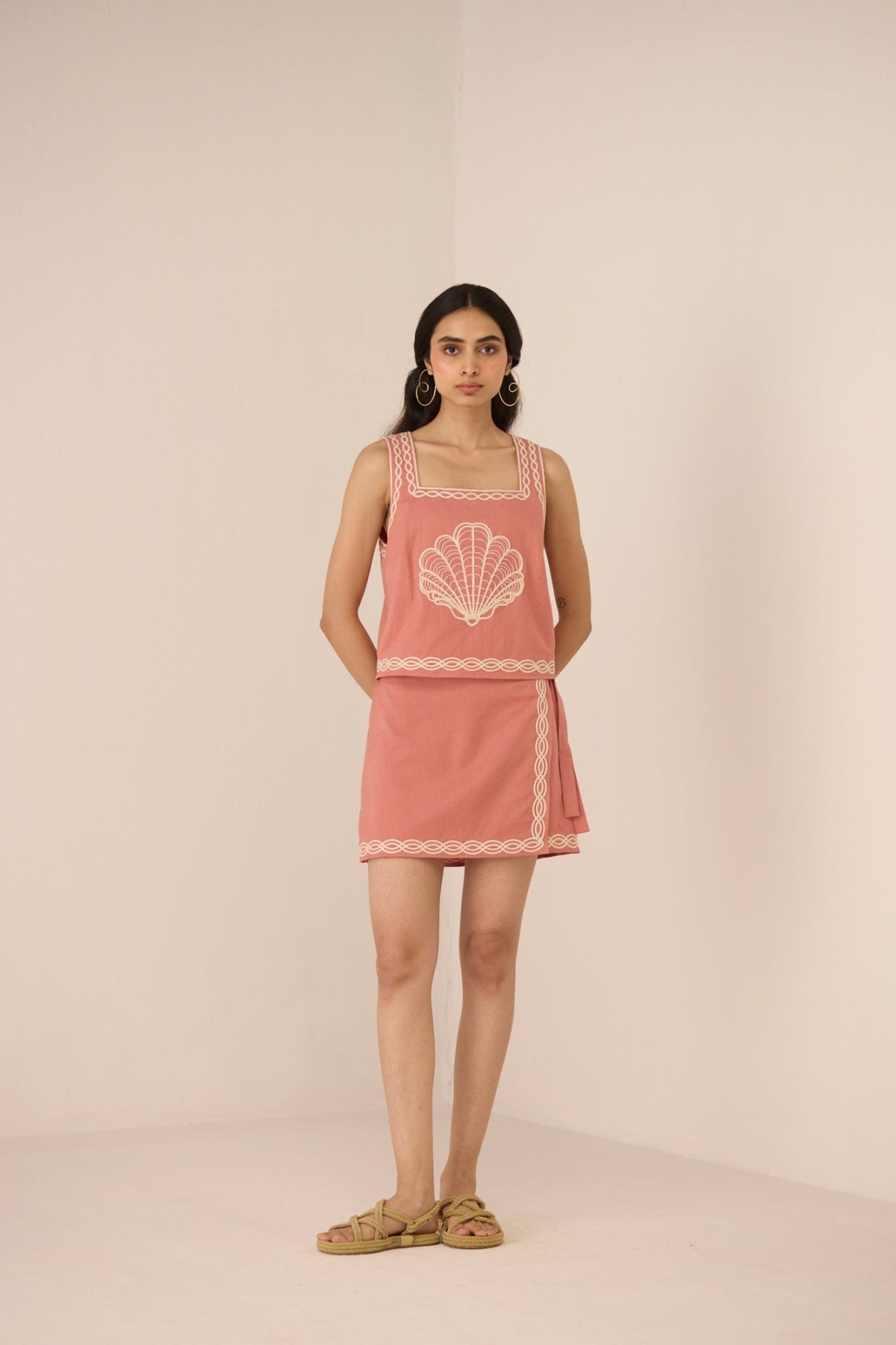 Woman wearing a pink dress with shell design on a beige background Calling June