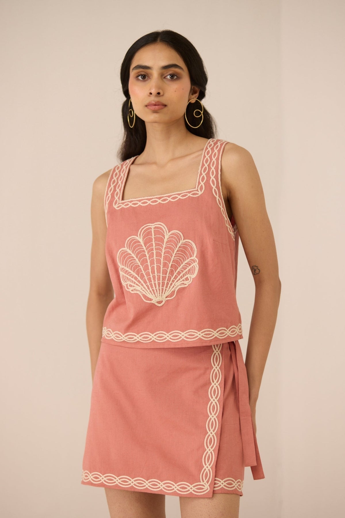 Woman wearing a pink dress with white shell design on a plain background Calling June