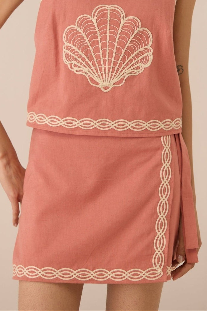 Woman wearing a pink dress with shell design on a beige background Calling June