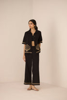 Woman wearing a black outfit with gold embroidery on a beige background Calling June