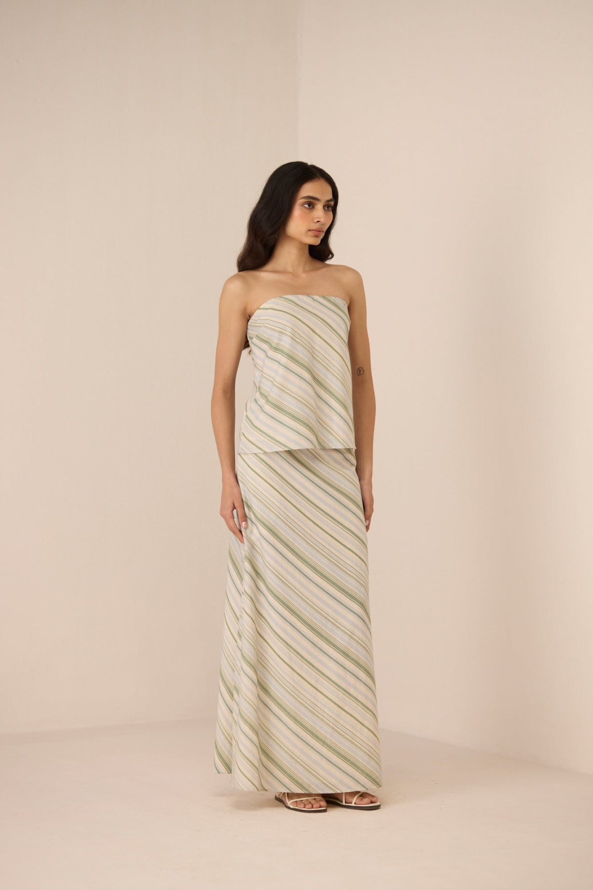 Woman wearing a strapless, long, patterned dress against a plain background Calling June