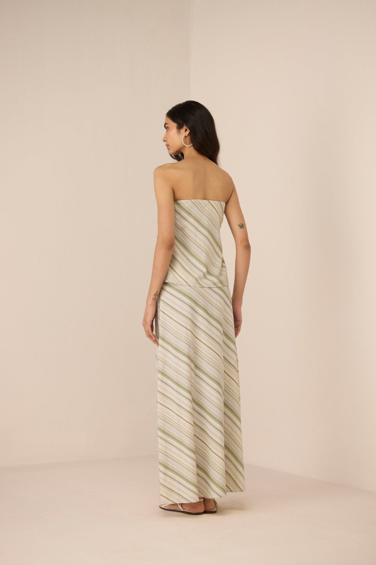 Woman wearing a strapless, long, striped dress against a plain background Calling June