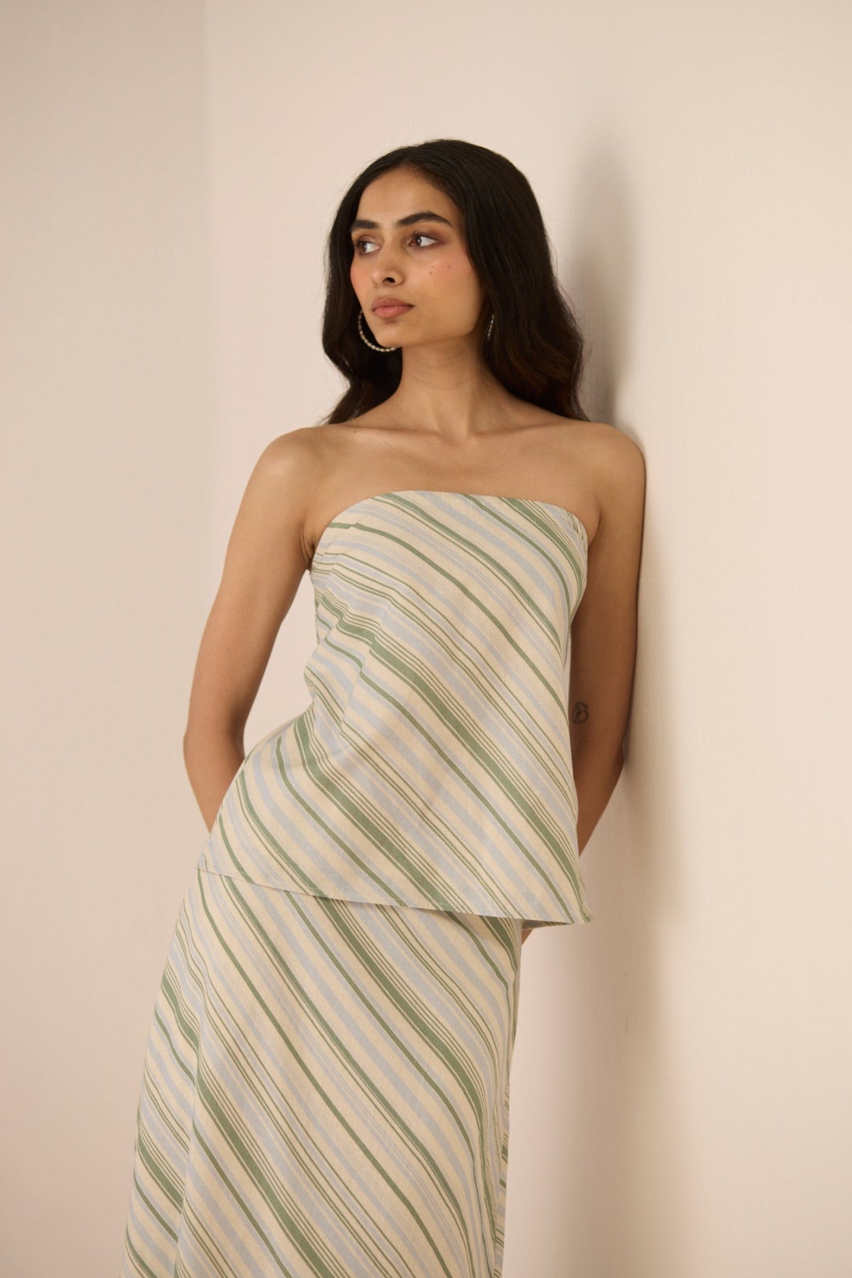 Woman wearing a strapless, green and white striped dress against a beige background Calling June