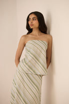 Woman wearing a strapless, green and white striped dress against a beige background Calling June