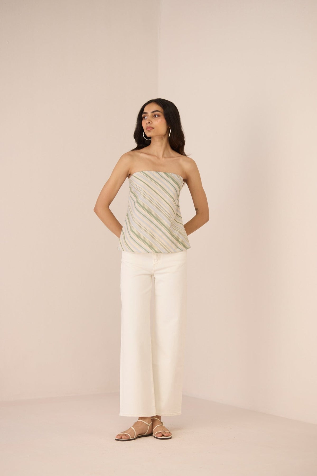 Woman wearing a strapless top and white pants against a beige background Calling June