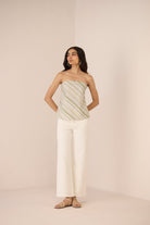 Woman wearing a strapless top and white pants against a beige background Calling June