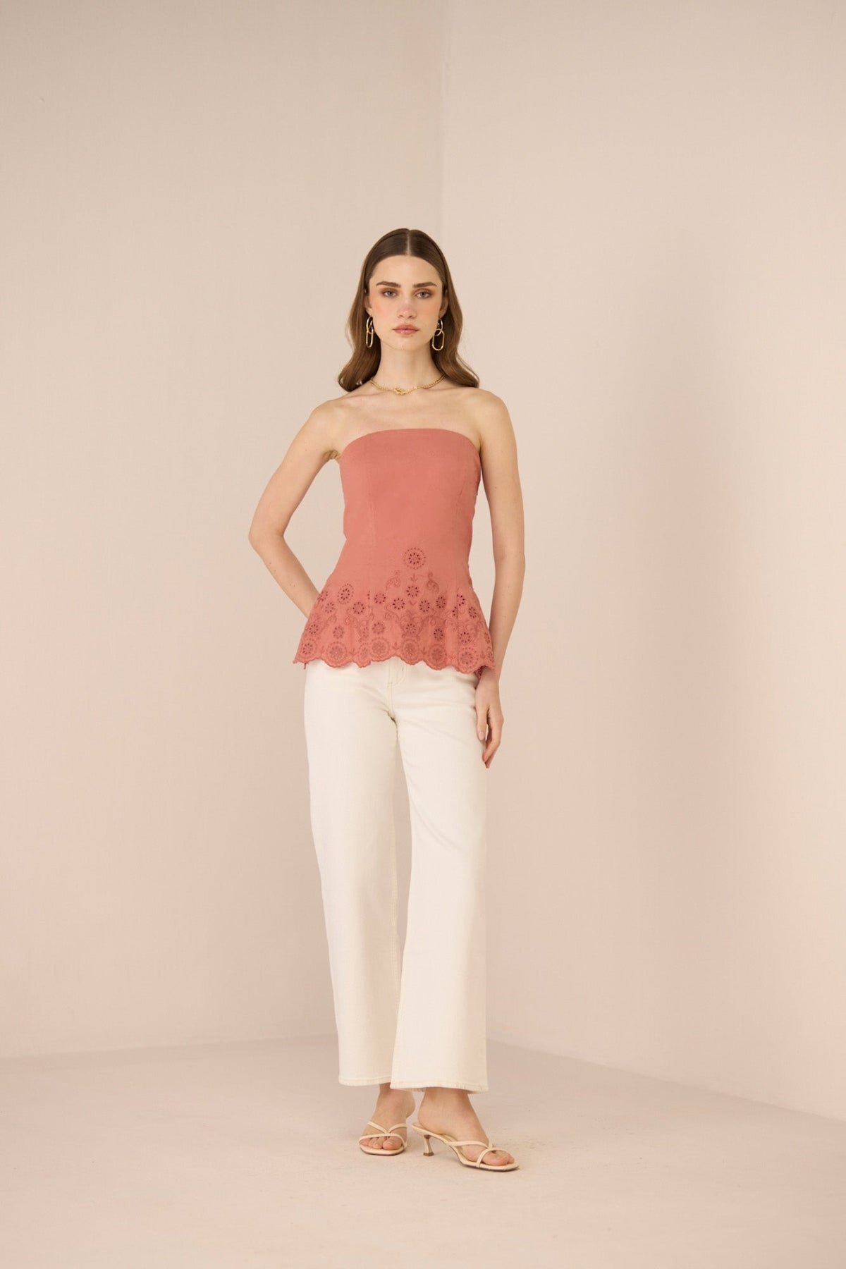 Woman wearing a pink strapless top with floral details and white pants on a beige background Calling June
