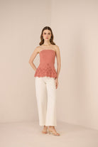 Woman wearing a pink strapless top with floral details and white pants on a beige background Calling June