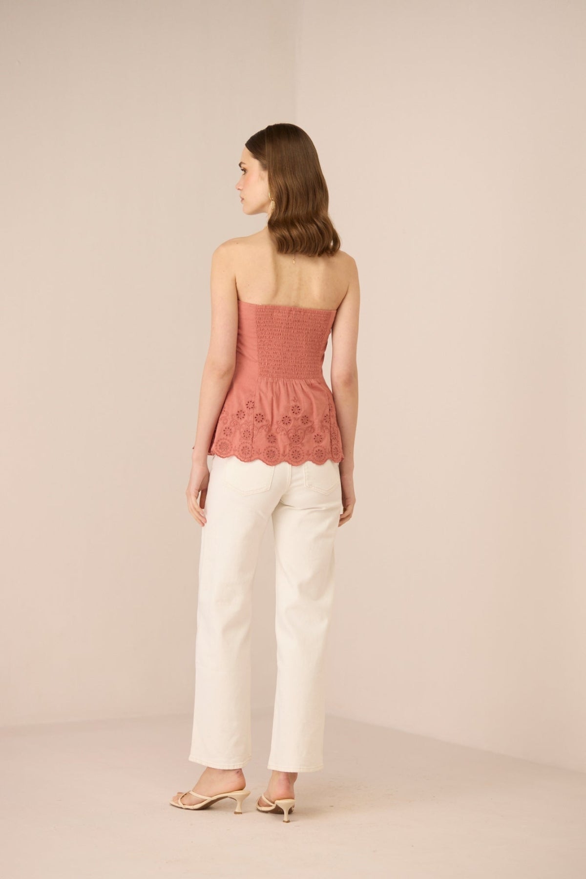 Woman wearing a pink strapless top and white pants on a beige background Calling June