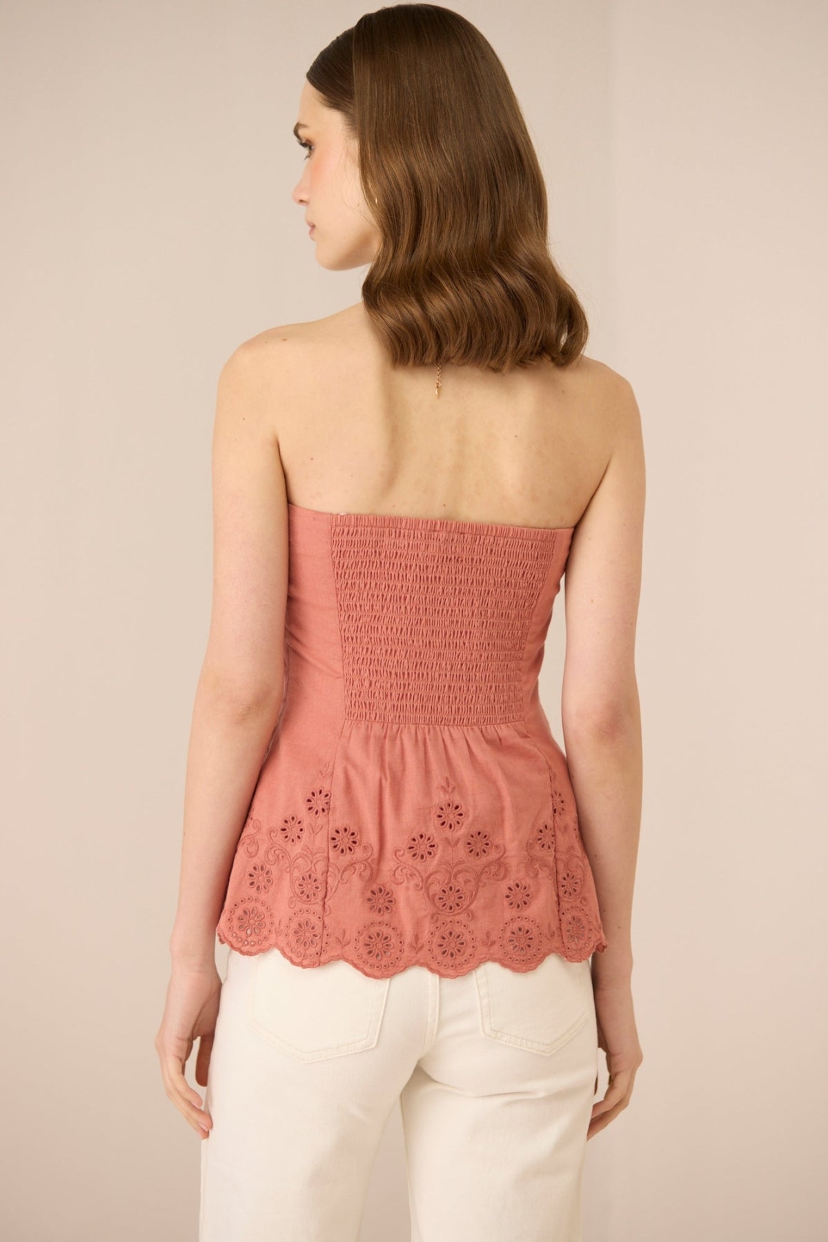 Woman wearing a pink strapless top with floral cut-out details on a beige background Calling June