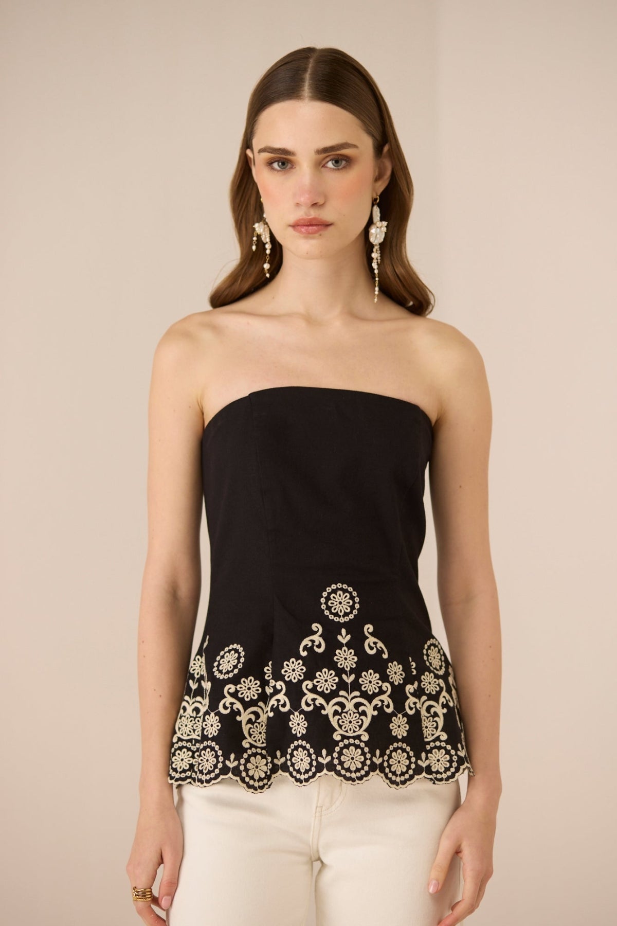 Woman wearing a black strapless top with white embroidery on a beige background Calling June